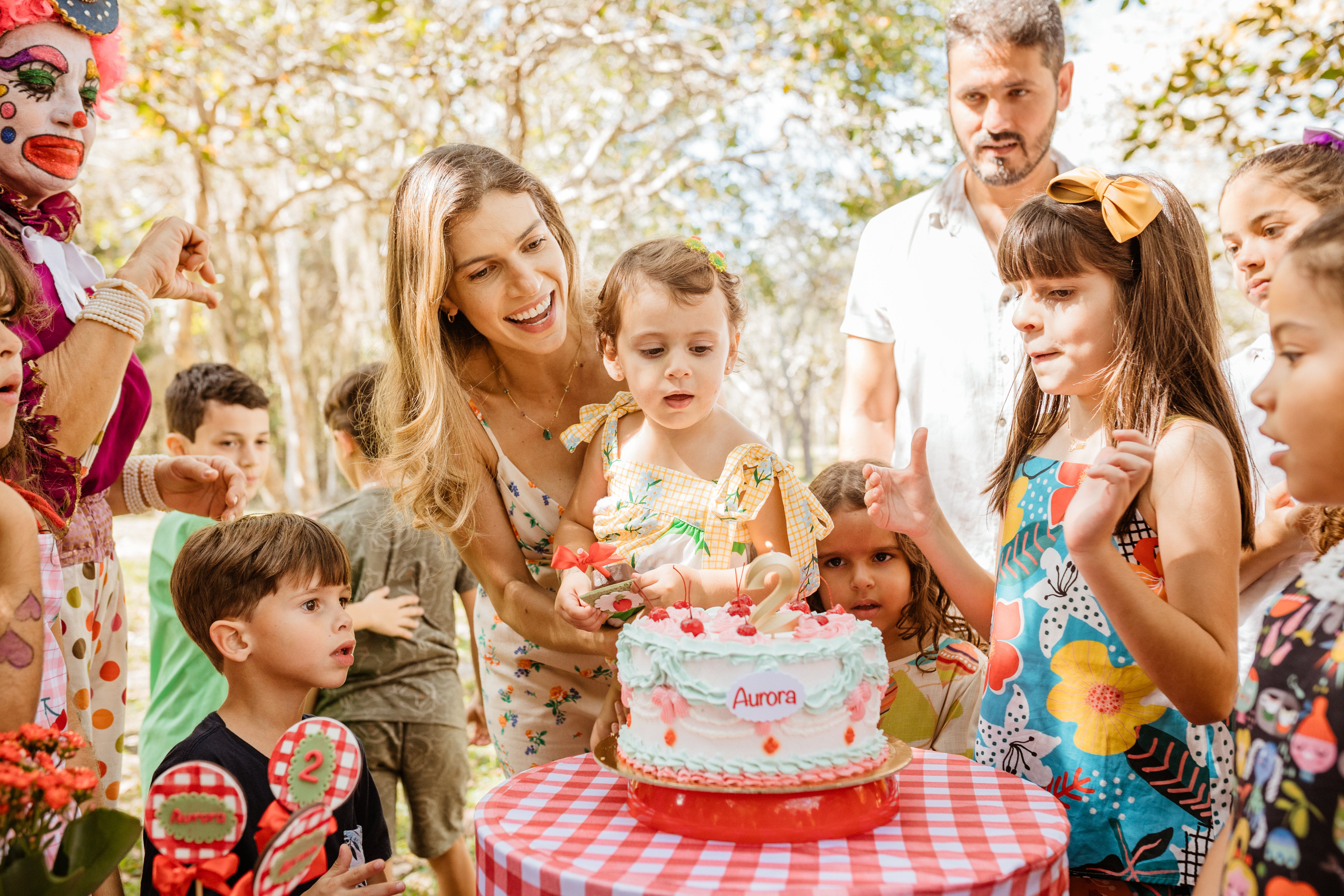 Child blowing out a candle on a cake at their birthday party. Parentings and children are gathered around the cake.