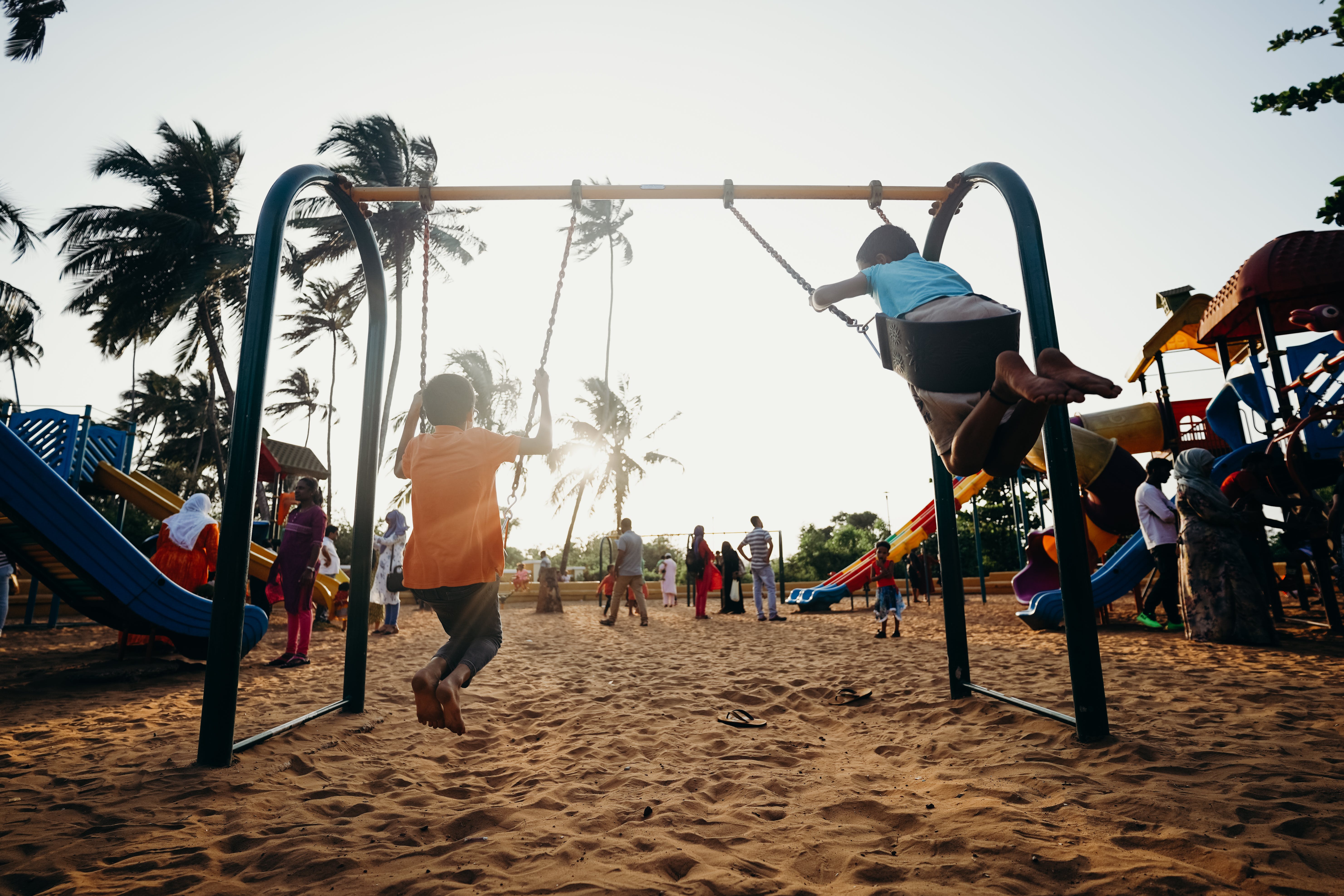 Highly sensitive children swinging on swings at the playground. There are many children and parents around.
