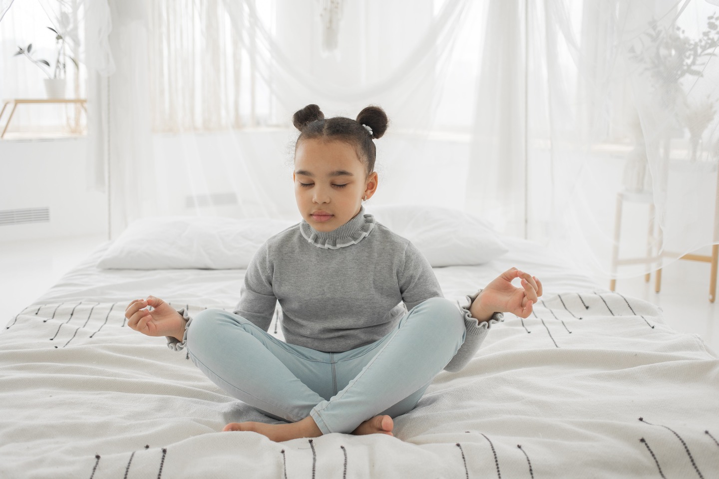 Highly sensitive young girl sitting criss-cross on her bed practicing calming breathing techniques