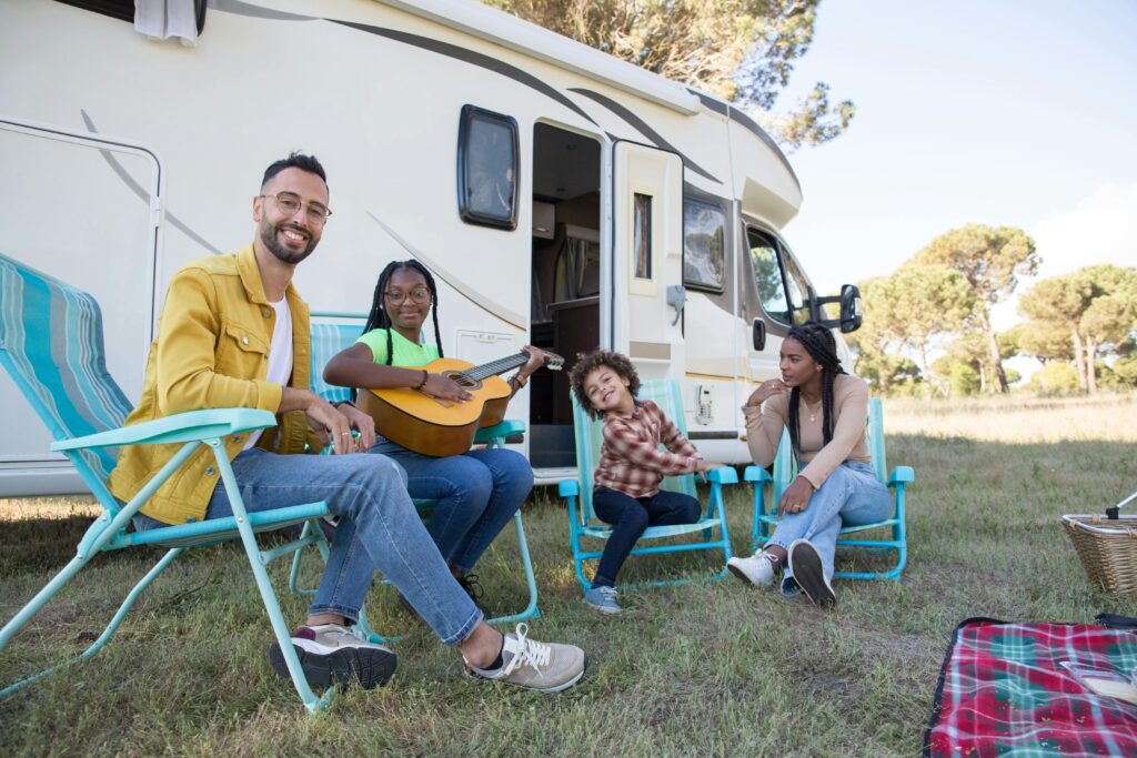 Family in front of an RV, sitting on lawn chairs, and smiling at the camera.